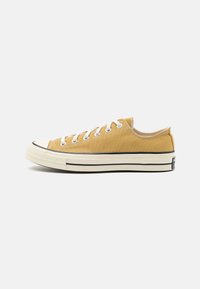 Lette sneaker i sennepsgul med hvite lisser, gummitåhette og svart detaljering på sålen. Uformell lavt design.