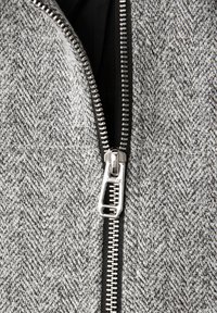 Šedá rybí kost tkanina s hladkou texturou, s lesklým stříbrným kovovým zipem vpředu a černou vnitřní podšívkou.