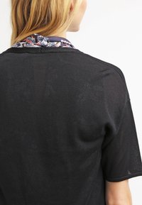 Svart stickad topp med korta ärmar, med en krage i blommönster i marinblått, rött och vitt. Texturerat tyg; avslappnad passform.