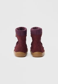 Botines de ante morados con un cuello de tela texturizada, cordones negros y suelas de goma marrones. Presenta un logo en relieve en el tacón.