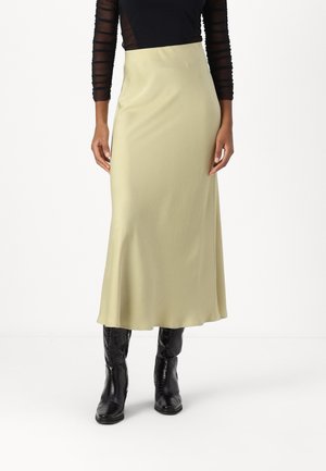 Maxi-Rock aus hellgrünem Stoff mit glatter Textur. Hat eine gerade Silhouette. Kombiniert mit schwarzen, strukturierten Ankle Boots.