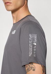 T-shirt sportivo grigio a maniche corte, con un accentuato dettaglio testurizzato sulle maniche e un motivo a contorno bianco con logo.