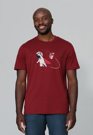 T-shirt en coton bordeaux avec un graphique d'un personnage portant un casque spatial et une cape, entouré d'étoiles et d'une planète. Manches courtes.
