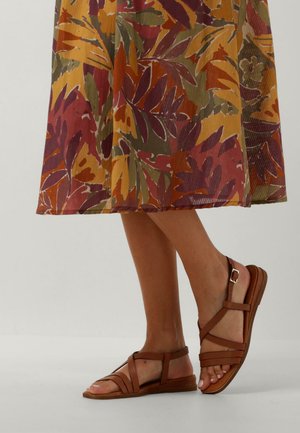 Bruine leren sandalen met meerdere banden en een gespsluiting. Platte zool en open ontwerp voor ademend vermogen. Gemaakt in combinatie met een rok met bloemenpatroon.