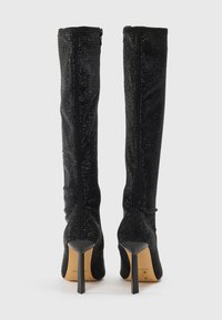Bottes noires hautes jusqu'aux genoux en tissu texturé avec des accents scintillants, présentant une silhouette épurée et des talons aiguilles droits et hauts.