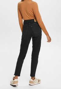 Zwarte spijkerbroek met hoogsluitend ontwerp, achterzakken en een bruin leren label. Gecombineerd met een nauwsluitende bruine top met lange mouwen en sneakers.