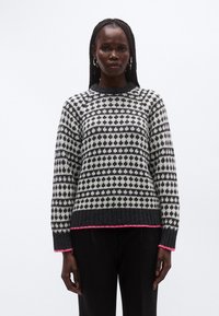 Stickad tröja med ett svartvitt geometriskt mönster, ribbade muddar och fåll, med kontrasterande rosa kant längs nederkanten.