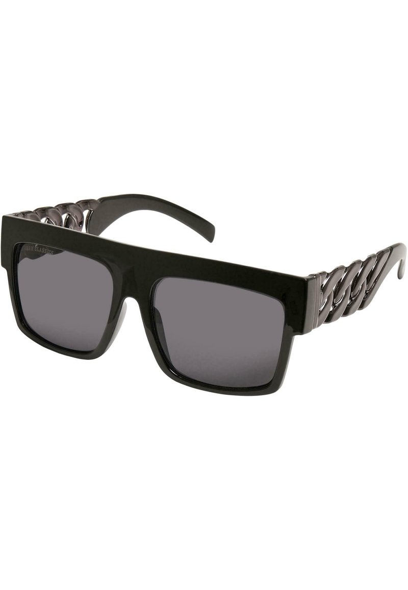 Occhiali da sole neri oversize con lenti scure. Presentano una montatura spessa e un design testurizzato simile a una catena metallica sulle tempie.