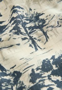 Textile présentant un design de paysage naturel en bleu foncé sur un fond beige, avec une texture visible et un matériau doux et tissé.