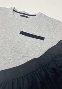 Szara koszulka z kieszenią wykończoną granatowym obszyciem oraz czarnym elastycznym paskiem z logo "WILD WOLF", o miękkiej fakturze i luźnym kroju.