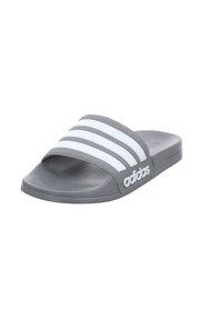 Sive Adidas natikače s tri bijele pruge preko remena, teksturiranom gumenom potplatom i zaobljenim oblikom za udobnost.