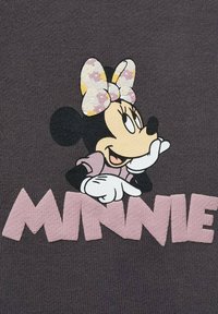 Tessuto grigio scuro con un personaggio dei cartoni animati stampato, che indossa un fiocco a pois, che punta al testo rosa "MINNIE" sottostante.