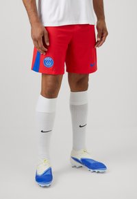 Røde og blå sportsbukser med et Paris-logo, parret med hvide sokker og blå fodboldstøvler med struktureret design og snørebånd.