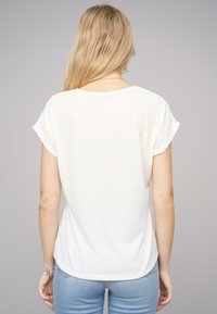 Haut blanc à manches courtes avec un col rond, texture douce et ourlet arrondi. Porté avec un jean bleu clair.