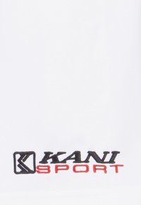 Bílá látka s hladkým povrchem, na levém dolním rohu vyšívané černé a červené logo s nápisem "KANI SPORT".