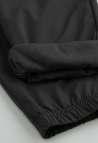 Czarna tkanina o gładkiej fakturze, wyposażona w elastyczny mankiet i marszczony dół. Prosty design bez widocznych wzorów czy elementów metalowych.