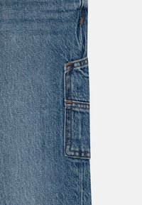 Jeans in denim blu chiaro con tasca laterale, cuciture standard e una texture leggermente sbiadita, con una vestibilità dritta.