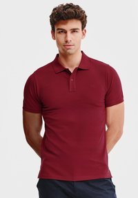 Bordowa koszulka polo z klasycznym kołnierzykiem, krótkimi rękawami i subtelnym logo. Wykonana z gładkiego, elastycznego materiału zapewniającego komfort.