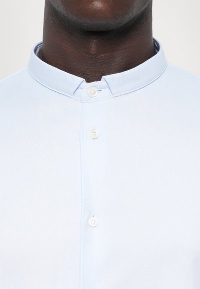Jasnoniebieska koszula z kołnierzykiem typu band, z trzema białymi guzikami z przodu i teksturowanym materiałem.