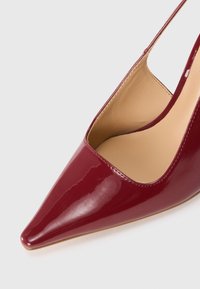 Scarpa slingback lucida bordeaux con punta appuntita e rivestimento interno beige, mostrata su uno sfondo chiaro e semplice.