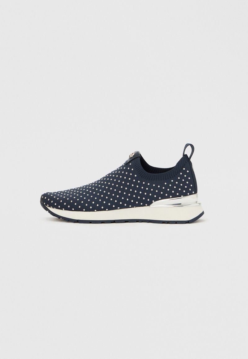 Baskets slip-on en tricot bleu marine avec des pois blancs, cheville rembourrée et accent argenté métallique au talon. Semelle flexible pour le confort.