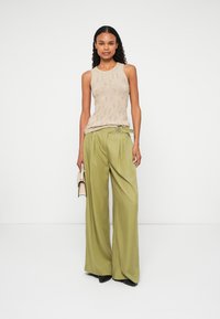 Μπεζ πλεκτό αμάνικο μπλουζάκι, ελαιόχρωμες φαρδιές παντελόνες με ζώνη και μία μικρή μπεζ τσάντα. Απαλή υφή, άνετη εφαρμογή, μινιμαλιστικό στυλ.