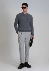 Grau gestrickter Pullover, hellgraue Hosen mit Falten, schwarze Schuhe und eine schwarze Clutch haltend. Glatte Textur mit klaren Linien.