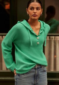 Roheline kootud kapuutsiga pluus, millel on tekstuuriline viimistlus, kootud nöör ja kolm dekoratiivset nööpi, millel on vabaltlangev lõige, koos teksashortsidega.