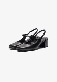 Sorte lær slingback-sko med firkantet tå, justerbar spænde og kraftig hæl. Glat tekstur med minimalistiske design detaljer.