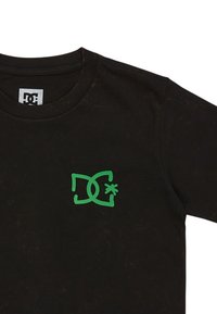 Svart bomullströja med rund hals, med en grön grafisk logotyp på vänster bröstområde. Mjuk känsla med lätta slitage märken.