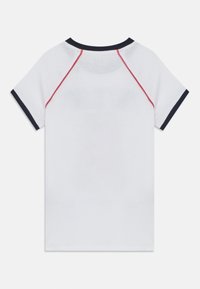 Camiseta blanca con mangas raglán y acentos en azul marino y rojo, textura suave y diseño de cuello redondo. Vista trasera solamente.