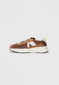 Braune und beige Sportschuhe aus Mesh und Wildleder, mit einem weißen Logo-Accent und strukturierten Schnürsenkeln vor einem weißen Hintergrund.