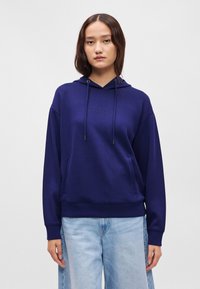 Námornícka modrá mikina s kapucňou vyrobená z jemného materiálu, s klokankou, sťahovacou kapucňou a diskrétnym vyšitým logom na hrudi.