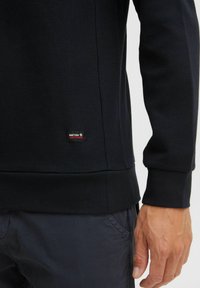 Pull noir avec un motif de tricot texturé et des poignets côtelés. Présente une petite étiquette de marque près de l'ourlet. Design à coupe ajustée.