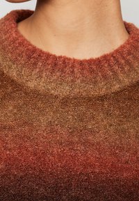 Suéter de punto con un cuello redondo acanalado que presenta un degradado de tonos terrenales desde el marrón hasta el óxido, mostrando una tela suave y texturizada.