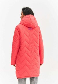 Korálová prešívaná parka s chevronovým vzorom, kapucňou a štítkom na krku. Má dlhé rukávy a rovný strih, vhodná do chladného počasia.