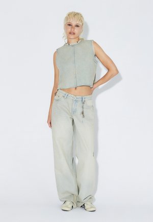 Leichte Jeans-Weste in Cropped-Form mit ärmellosem Design und rohem Saum, kombiniert mit locker sitzenden hellblauen Jeans mit dekorativem Kettenakzent.