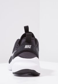 Svart idrottssko med övre i tyg, vit sula, framträdande Nike-logotyp och en dragflik vid hälen för enkel påtagning.