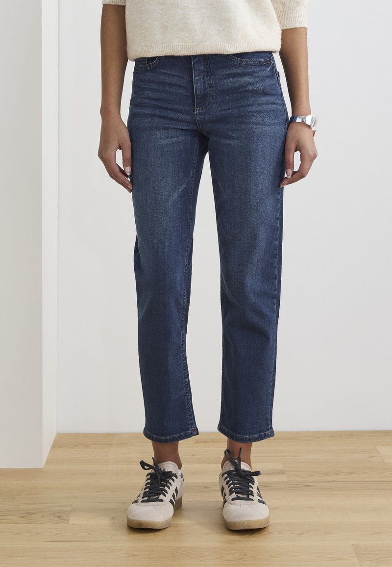 Jean en denim d'un bleu foncé, avec une coupe droite, une taille mi-haute et un délavage subtil. Associés à des baskets claires.