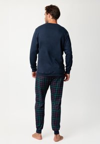 Camiseta de manga larga de color navy combinada con pantalones de pijama de cuadros que presentan líneas verdes y rojas sobre un fondo oscuro. Material de algodón suave.