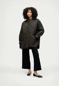 Vadderad mörkbrun jacka med avslappnad passform, utrustad med hög krage, framdragkedja och två sidofickor, kombinerad med svarta vida byxor och platta skor.