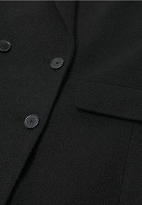 Musta herringbone-kankaasta valmistettu bleiseri, jossa on kaksi mustaa nappia ja yksi tasku. Pehmeä pinta ja klassinen räätälöity muotoilu.