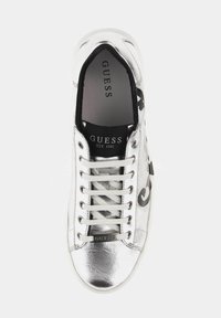 Baskets métalliques argentées avec lacets blancs, présentant un logo noir sur le côté et une texture lisse. La marque est visible sur la semelle intérieure.