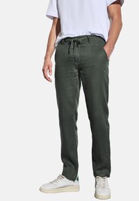 Vihreät pellavahousut, joissa on rento malli, narukiristysvyötärö ja sivutaskut, yhdistettyinä valkoisiin lenkkitossuihin ja yksinkertaiseen valkoiseen t-paitaan.