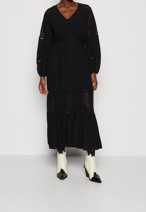 Czarna sukienka z długim rękawem, z koronkowymi panelami, dekoltem w serek i zapięciem na guziki. Posiada warstwową spódnicę i teksturowany materiał. Noszona z dwutonowymi botkami.