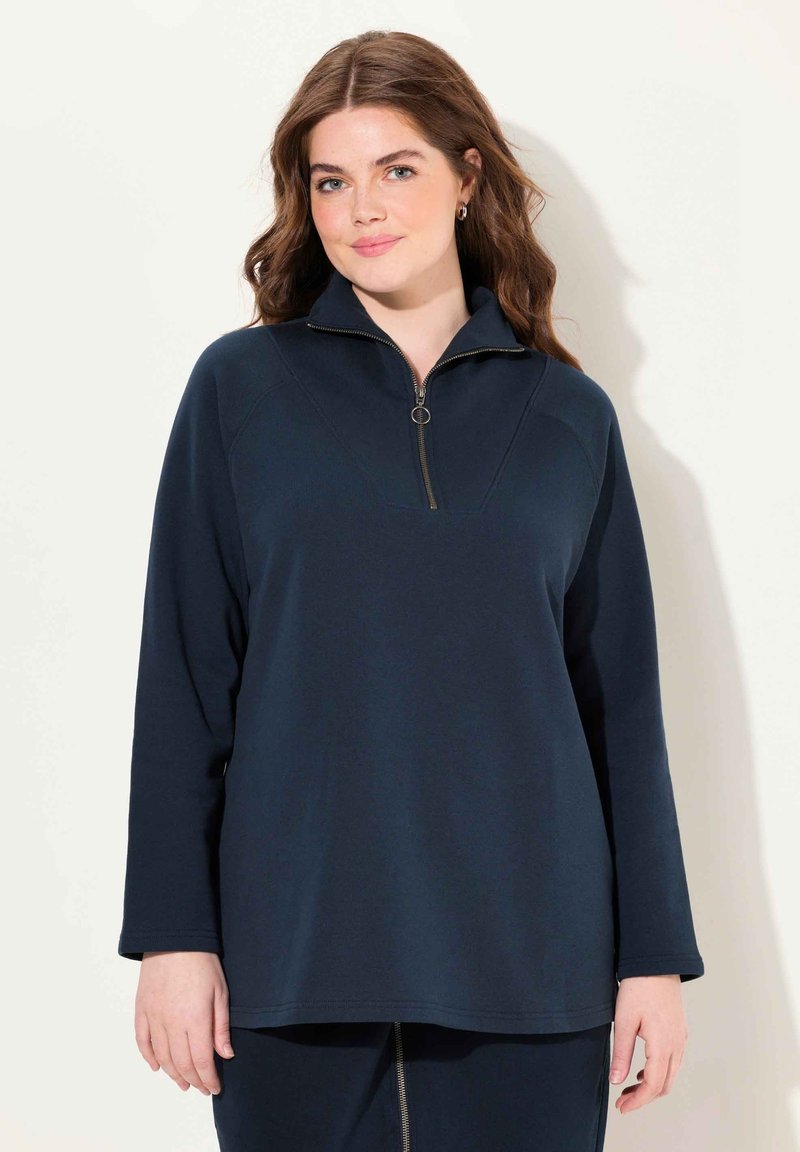 Marinblå zip-up sweatshirt med kvartslång dragkedja, avslappnad passform, långa ärmar och slät textur. Har en v-formad sömdetalj.