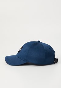 Tumed sinine baseballi müts, millel on kõver ääreosa, tekstureeritud kangas ja must logopael ees. Tagaküljel on reguleeritav rihm.
