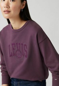 Fioletowa bluza z dużym haftowanym logo "LEVI'S" oraz okrągłym wzorem. Wykonana z miękkiej, teksturowanej tkaniny z prążkowanymi mankietami.