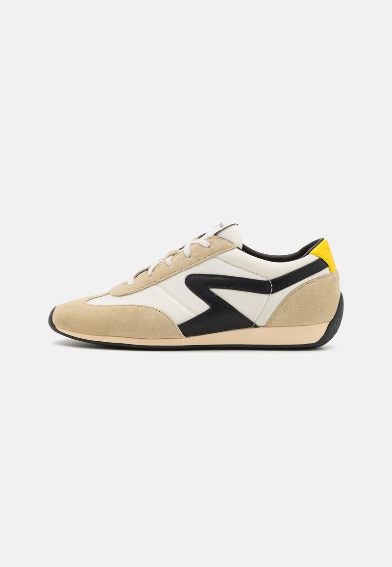 Beige and white athletic shoes with black accents and yellow heel. Suede and leather materials, rounded shape, flat sole, and lace closure.