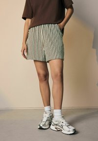 Gestreifte grüne und braune Shorts mit elastischem Bund, kombiniert mit weißen Socken und silbernen Sneakers. Glattes Material mit horizontalen Linien.